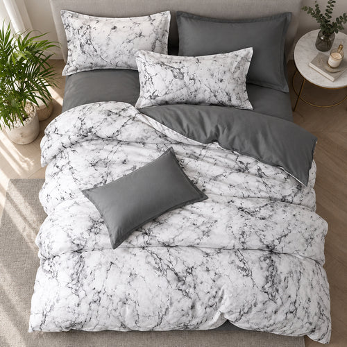 Marble-patterned bedding set on a bed with decorative pillows and a plant.